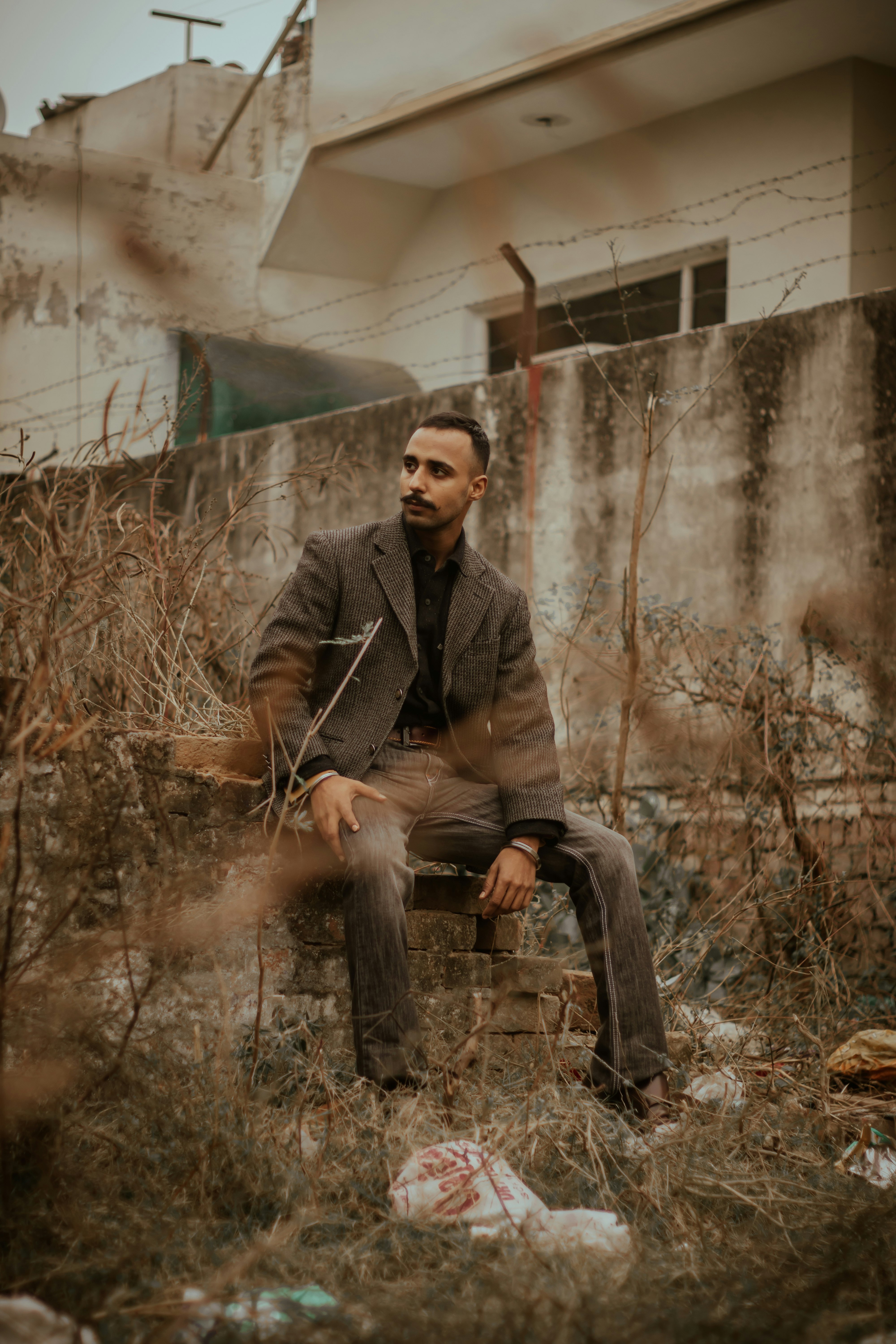 man in brown coat sitting on brown dried leaves during daytime